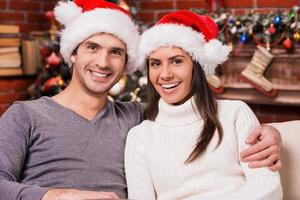 liefde is de het beste geschenk. mooi jong liefhebbend paar bonding naar elk andere en glimlachen met Kerstmis boom in de achtergrond foto