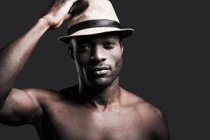 mijn Lucky hoed. portret van jong zonder shirt Afrikaanse Mens aanpassen zijn hoed en op zoek Bij camera terwijl staand tegen grijs achtergrond foto