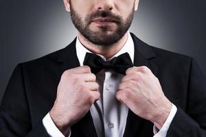 perfect stijl. detailopname van knap volwassen Mens in formele kleding aanpassen zijn boog stropdas terwijl staand tegen grijs achtergrond foto