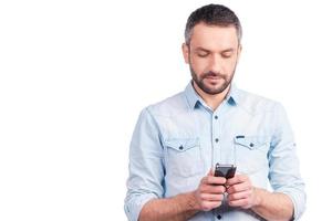 Mens sms'en. zelfverzekerd jong Mens in gewoontjes slijtage typen iets Aan zijn slim telefoon terwijl staand geïsoleerd Aan wit achtergrond foto