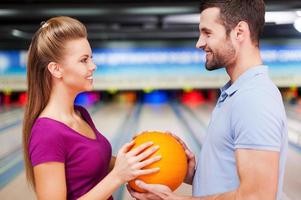 in liefde tegen de achtergrond van bowling steegjes. vrolijk jong paar op zoek Bij elk andere en Holding bowling ballen terwijl staand tegen bowling steegjes foto