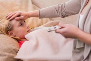 ik hoop het is niet griep. moeder Holding thermometer en aanraken voorhoofd van haar ziek dochter aan het liegen Aan de bankstel foto