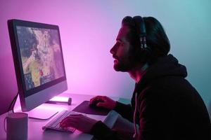 silhouet van Mens op zoek Bij de computer toezicht houden op terwijl spelen spel tegen kleurrijk achtergrond foto