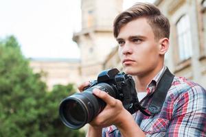 klaar naar schieten. knap jong Mens Holding digitaal camera en op zoek weg terwijl staand buitenshuis foto