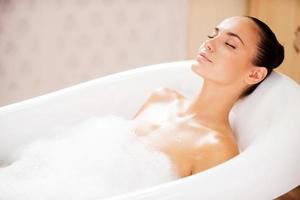 schoonheid in bubbel bad. kant visie van aantrekkelijk jong vrouw houden ogen Gesloten terwijl genieten van luxueus bad foto
