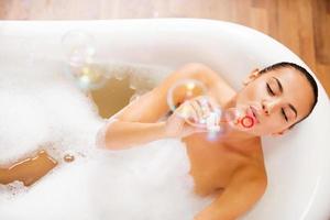 bubbel plezier. top visie van mooi jong vrouw blazen zeep bubbels terwijl genieten van bubbel bad foto