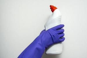 een hand- in een Purper rubber schoonmaak handschoen houdt een plastic fles van wasmiddel foto