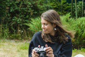 schattig tiener meisje met een camera, een meisje nemen afbeeldingen Aan een retro wijnoogst camera Aan de gras in de park, een hobby concept foto