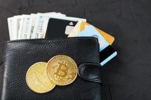een zwart portemonnee met dollar, e-kaarten en bitcoins Aan een zwart getextureerde achtergrond. foto