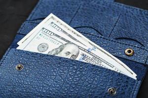handtas van blauw kleur van oprecht leer met nieuw een honderd dollar rekeningen Aan een zwart achtergrond. foto