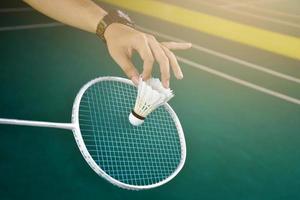 badminton speler houdt racket en wit room shuttle in voorkant van de netto voordat portie het naar een ander kant van de rechtbank. foto