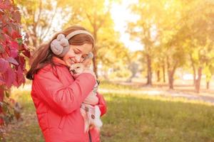 een tiener- meisje in een oranje jasje met een chihuahua hond in haar armen. de meisje knuffels haar hond. foto