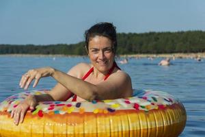 schattig jong vrouw met kleurrijk opblaasbaar zwemmen cirkel zwemt in de blauw water van de zee Aan een heet zonnig dag foto