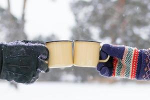 twee metaal cups met heet thee in handen Mens en vrouw Aan een achtergrond van winter Woud. foto