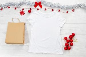 dichtbij omhoog wit blanco sjabloon t overhemd met kopiëren ruimte papier tas. Kerstmis vakantie concept. top visie mockup t-shirt, ster, wit houten achtergrond. gelukkig nieuw jaar decoraties accessoires. Kerstmis kleding foto