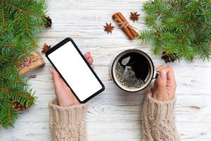 vrouw handen Holding modern smartphone met moskee omhoog en mok van koffie Aan houten tafel met Kerstmis decoratie. top visie foto