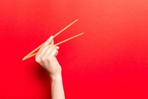 creatief beeld van houten eetstokjes in vrouw hand- Aan rood achtergrond. Japans en Chinese voedsel met kopiëren ruimte foto