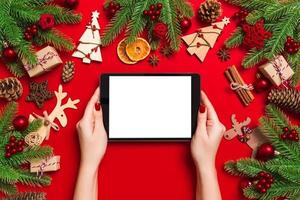 top visie van vrouw Holding tablet in haar handen Aan rood achtergrond gemaakt van Kerstmis decoraties. nieuw jaar vakantie concept. mockup foto