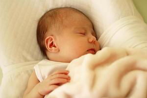 schattig pasgeboren baby slapen Aan een wit bed onder beige deken. foto