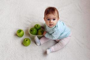 weinig meisje is zittend Aan een wit plaid met groen appels. concept van gezond voedsel voor zuigeling kinderen. foto