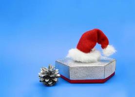zilver geschenk doos met de kerstman claus hoed en pijnboom ijshoorntje Aan blauw achtergrond. kerstmis, nieuw jaar. kopiëren ruimte foto