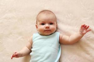 schattig zuigeling baby in blauw bodysuit is aan het liegen Aan een beige deken. foto