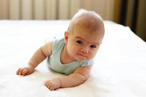 weinig schattig baby meisje is proberen naar kruipen Aan een bed Bij huis. foto