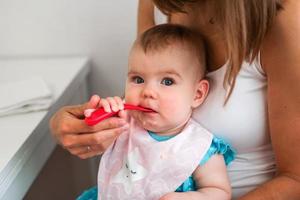 moeder voeden schattig baby meisje groente puree van een lepel. gezond aan het eten voeding voor weinig kinderen foto