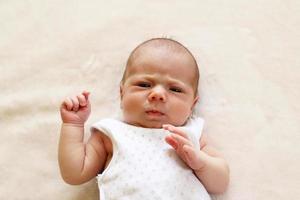 schattig een maand baby ernstig op zoek Bij de camera Aan een beige deken. foto