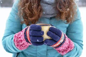 dames handen in breiwerk kleurrijk handschoenen zijn Holding metaal kop met heet thee in winter park. foto