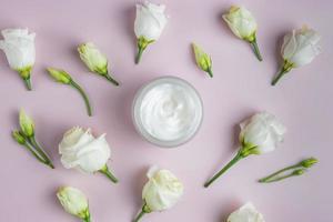 top visie van Open pot met gezicht proppen omringd verspreide bloeiend Eustoma bloemen. huid zorg schoonheidsmiddelen presentatie. foto