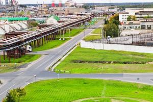 industrieel landschap. panoramisch visie van de technologisch pijpen. fabriek instellingen. van de chemisch rood Wit pijpen rook is komt eraan. productie gebouwen. tegen achtergrond van lucht en helder gras foto