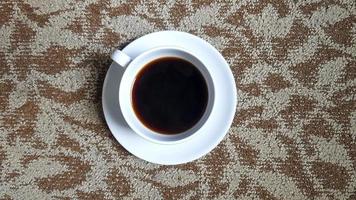 top visie van wit kop van zwart koffie Aan bruin tapijt of tapijt achtergrond met kopiëren ruimte. vlak leggen van heet drinken Aan katoen verdieping behang. foto