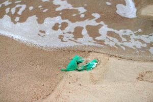 leeg gebruikt plastic groen zak Aan zee zanderig kust foto