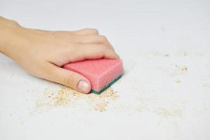 keukentafel schoonmaken. roze spons in de hand van de vrouw verwijdert vuil, broodkruimels en restjes. huishoudelijke taken foto