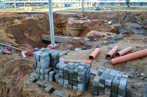 asfalt bakstenen liggen Bij een bouw plaats. klein grijs bakstenen zijn gestapeld vlak Aan een bouw plaats in de stad centrum. dichtbij zijn metaal pijpen en een zand gleuf. groot bouw plaats foto