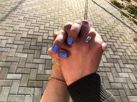 meisje en vent houden handen. de meisjes nagels zijn gedekt met blauw-zilver vernis en ze is vervelend een goud armband. mooi en elegant manicuren. seks en de stad foto