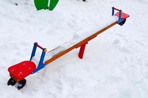 kinderen klein speelgoed- schommel balancer gedekt met sneeuw Aan een kinderen speelplaats in de winter foto