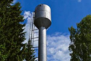 groot ijzer metaal glimmend roestvrij industrieel water toren voor leveren water met een groot capaciteit, vat tegen de blauw lucht en bomen foto