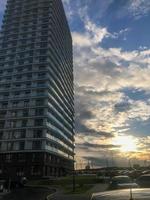 hoog woon- blok van appartementen, kolom in de stad centrum. huis van een nieuw formaat, wit, zonder een balkon met een glas terras en veel ramen. tegen de achtergrond van een helder zonnig lucht foto