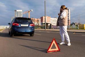 een vrouw bestuurder Aan een snelweg De volgende naar een gebroken naar beneden auto pratend Aan een mobiel telefoon De volgende naar een noodgeval hou op driehoek, weg veiligheid concept foto