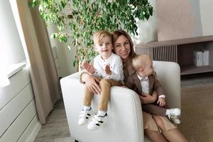 elegant jong moeder met twee klein kinderen op zoek Bij de camera met een glimlach zittend in een stoel foto