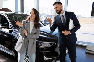 een jong vrouw in een auto dealer, samen met een medewerker, een auto handelaar kiest een nieuw auto. auto verhuur concept foto