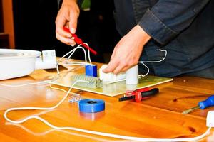 een Mens werken elektricien werken, verzamelt de elektrisch stroomkring van een groot wit straat lamp met draden, een relais Bij een industrieel fabriek fabriek foto