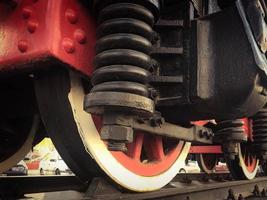 groot ijzer wielen van een rood en zwart trein staand Aan rails en suspensie elementen met veren van een oud industrieel stoom- locomotief foto
