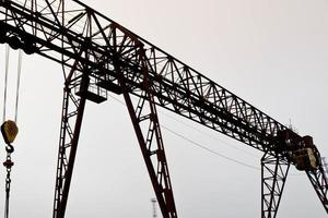 industrieel ijzer groot metaal portaal kraan met een haak gemonteerd Aan de ondersteunt voor hijs- en draag- zwaar lading, in beweging langs de rails Bij de fabriek. de kraan is van brug type foto