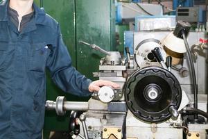 een Mens werken in een gewaad, overall staat De volgende naar een industrieel draaibank voor snijden, draaien messen van metalen, hout en andere materialen, draaien, maken details en Reserve onderdelen Bij de fabriek foto