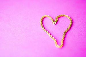 structuur van een mooi gouden feestelijk keten uniek het weven in de vorm van een hart Aan een roze Purper achtergrond en kopiëren ruimte. concept liefde, huwelijk voorstel, huwelijk, st. Valentijnsdag dag foto