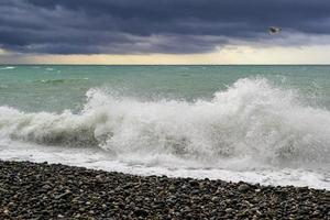 spatten van golven gedurende stormachtig wind in de zee Bij kiezelsteen strand. foto