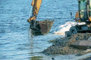 graafmachine werken naar versterken de dijk. hydraulisch graafmachine werken Aan de rivier- bank. foto